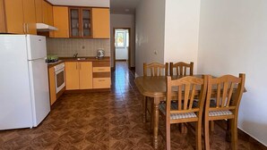 Una cocina con armarios de madera, un refrigerador blanco, una mesa de comedor con sillas y piso de baldosas.