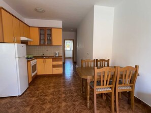 A kitchen with wooden cabinets, a white refrigerator, a dining table with chairs, and a tiled floor.