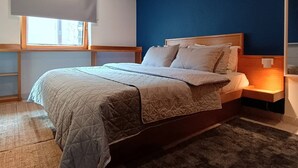 Un dormitorio con cama, mesita de noche, ventana con persianas y una pared de acento azul.