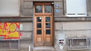 Fachada de edificio con puerta doble de madera, portón metálico y ventana a nivel de calle.
