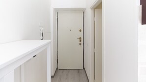 Un corridoio stretto con una porta bianca in fondo, una parete bianca e un pavimento chiaro.