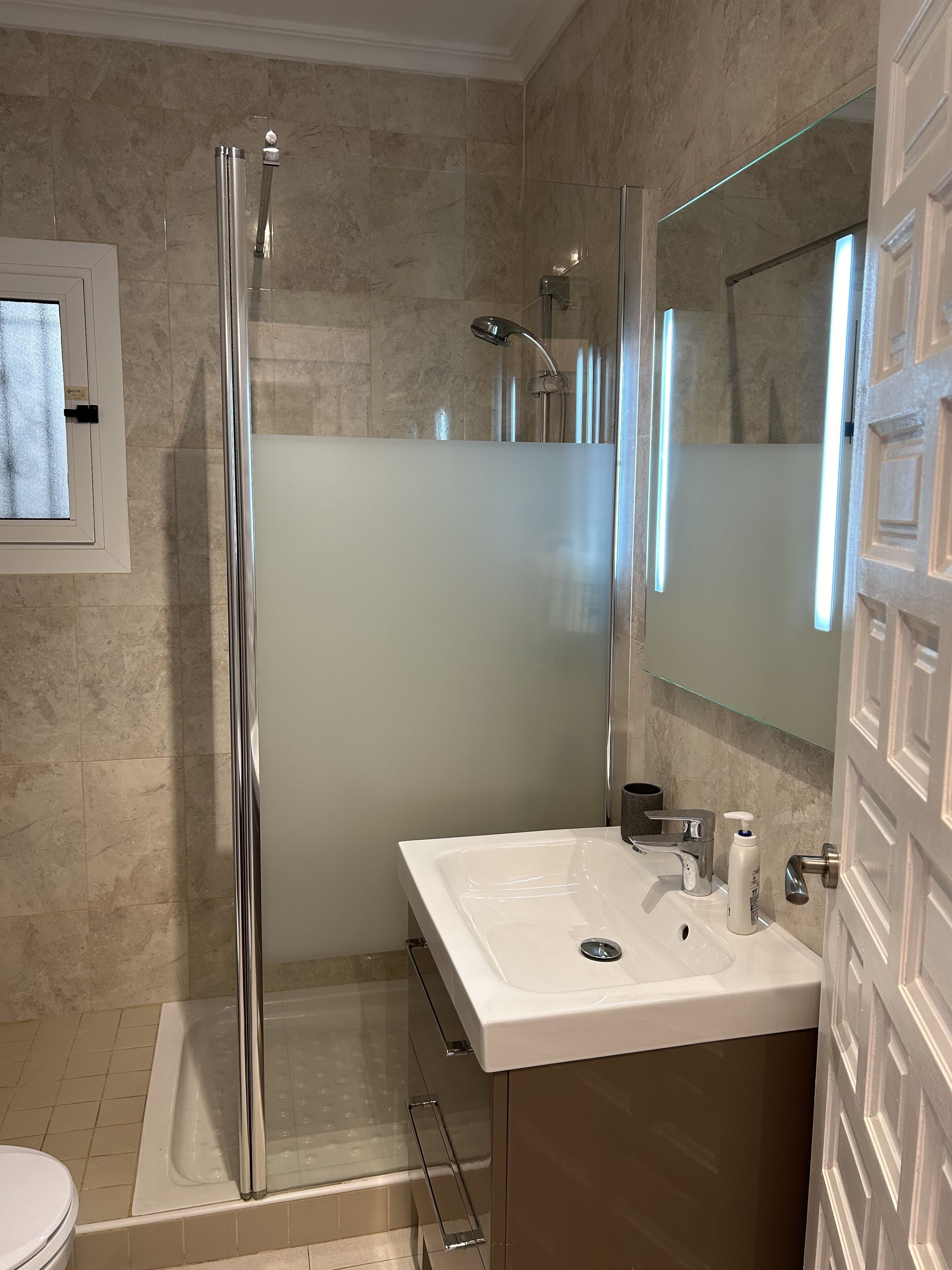 A modern bathroom with a glass-enclosed shower, a white sink with a mirror above it, and a toilet.