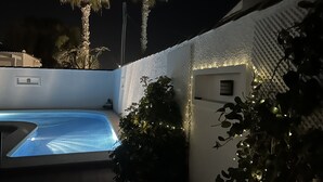 Una piscina con pared texturizada e iluminación colgante, rodeada de vegetación y palmeras.