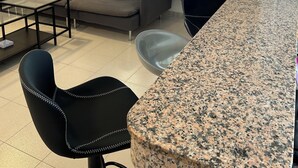 Una sala de estar con sofá, una mesa de centro, una zona de comedor con encimera de granito y sillas, y una ventana con cortinas azules.