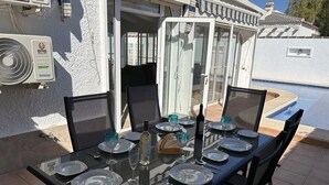 Un área de comedor al aire libre con una mesa de vidrio preparada para seis personas, rodeada de sillas, cerca de una piscina.