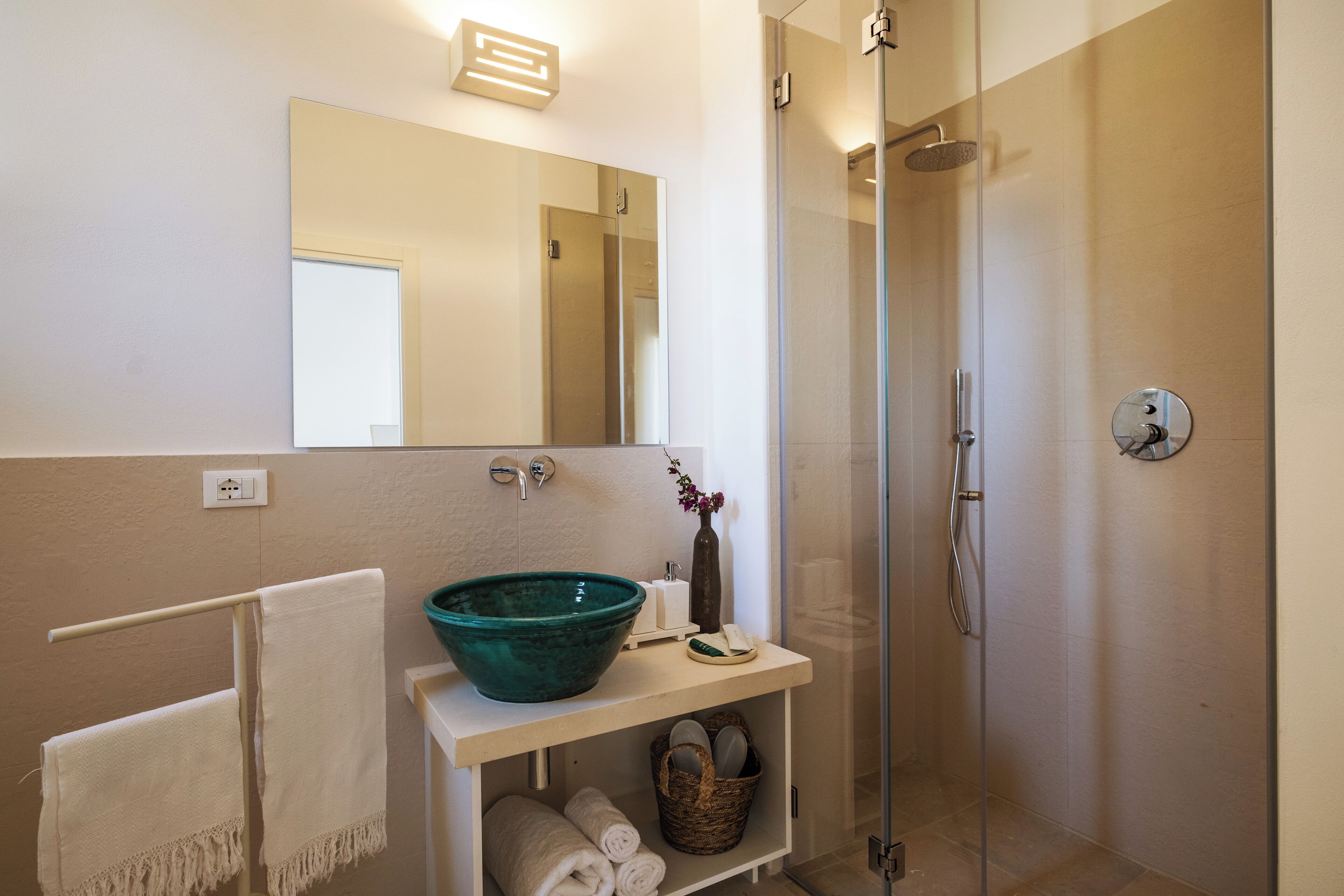 Un baño con un espejo grande, un lavabo con un recipiente verde, una ducha y un perchero para toallas.
