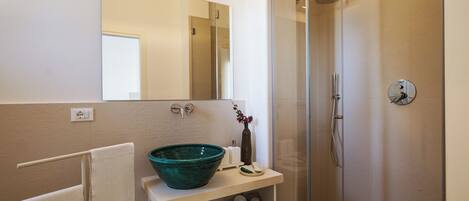 Un baño con un espejo grande, un lavabo con un recipiente verde, una ducha y un perchero para toallas.