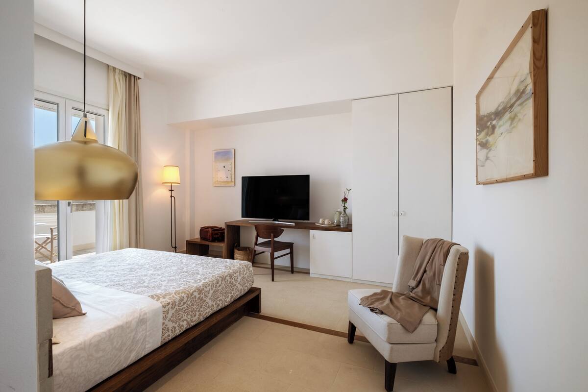 A modern hotel room with a bed, a desk, a television, and a chair.