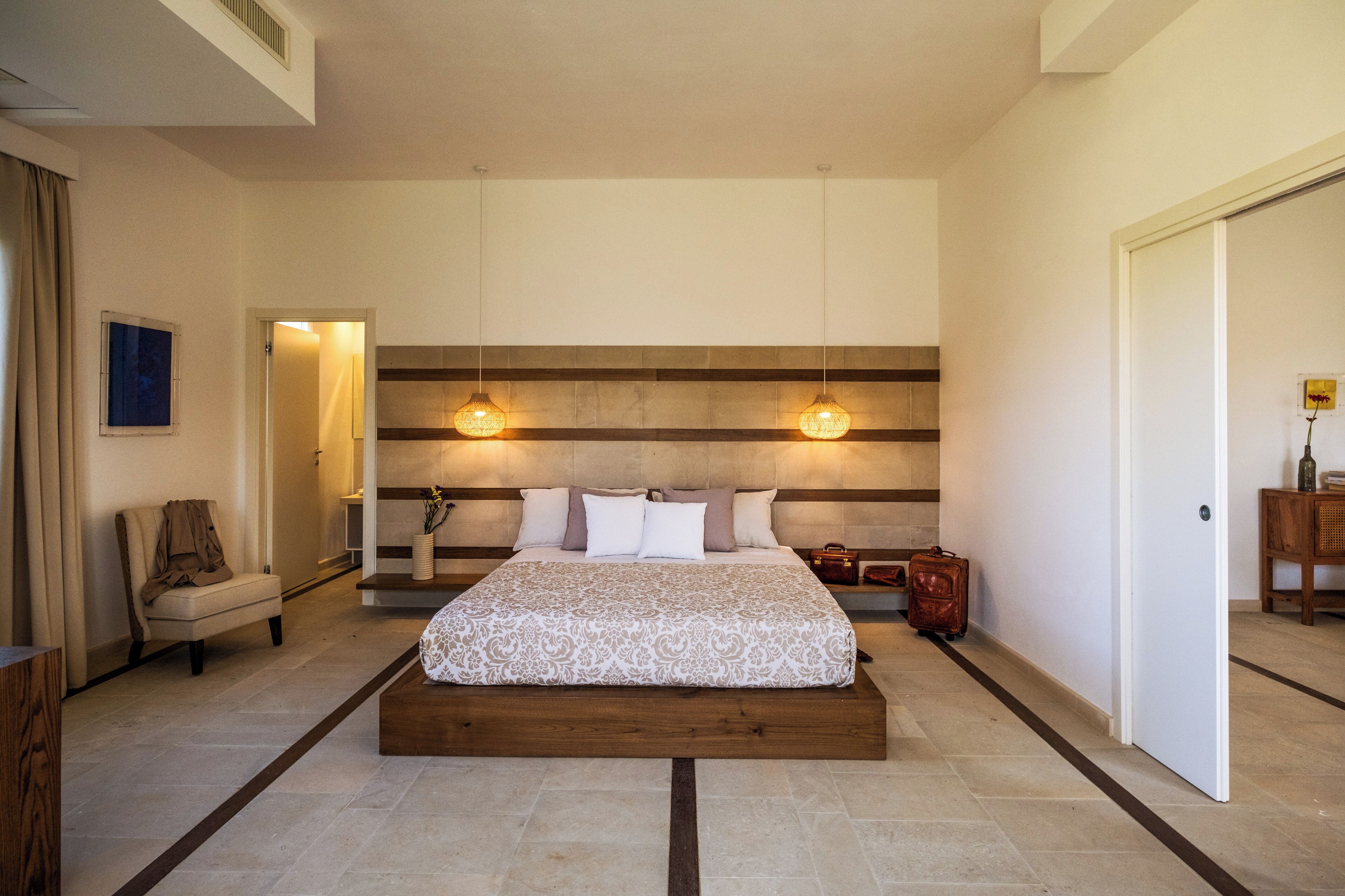 A bedroom with a large bed, bedside tables, a chair, and a suitcase.