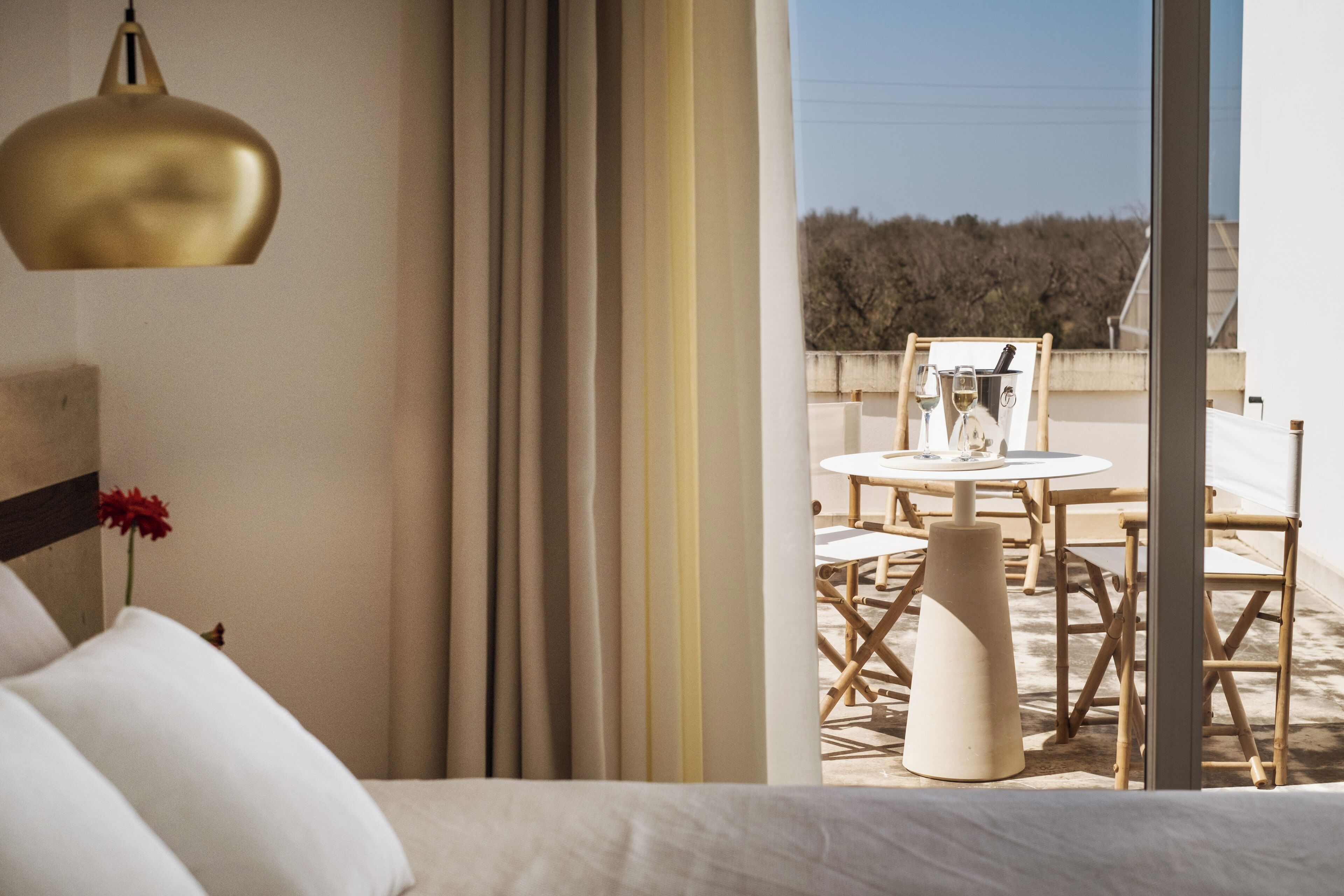 A hotel room with a bed, a large window, and a balcony with a table and chairs.