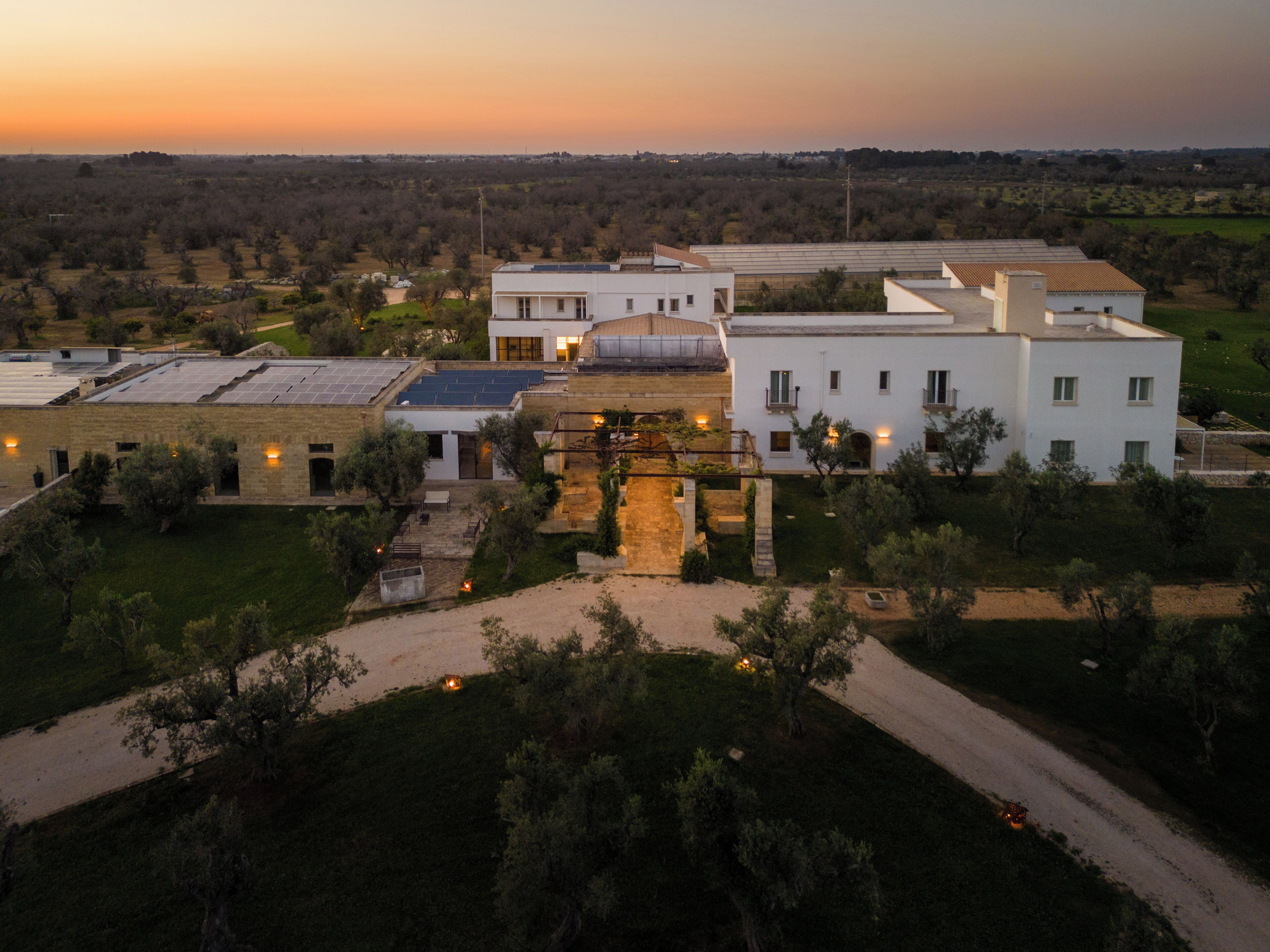 A modern building with multiple white structures, a paved courtyard, and surrounding greenery.
