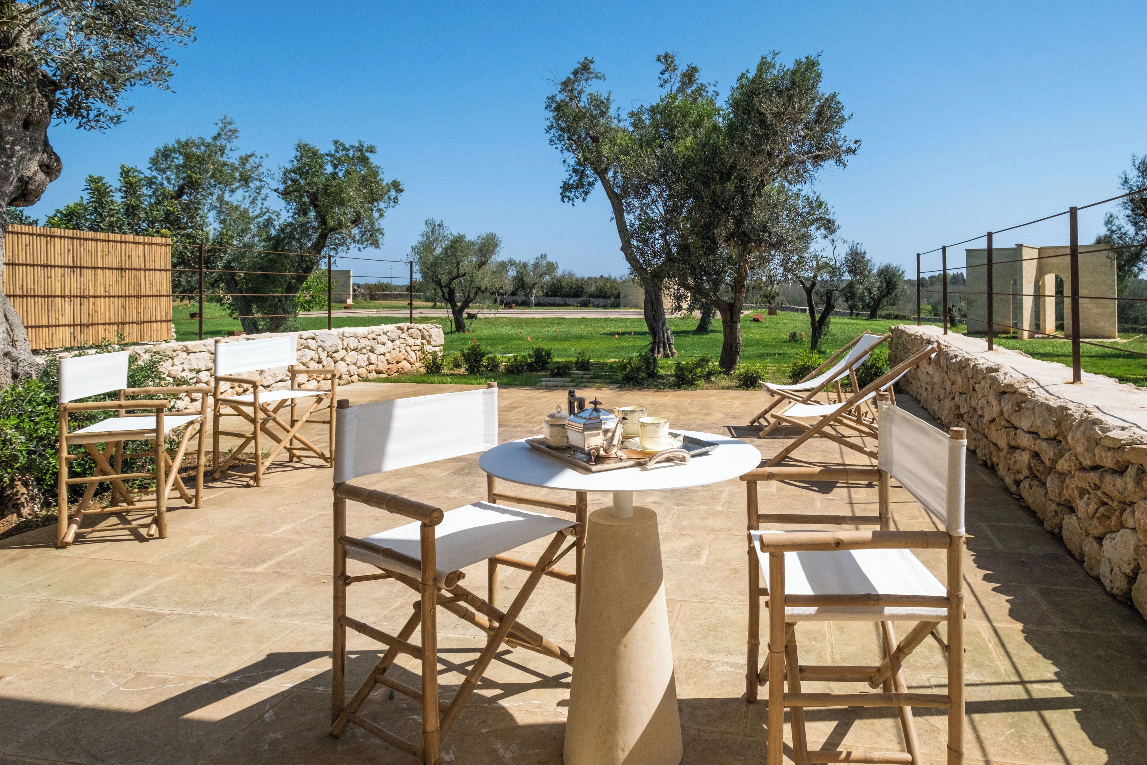 An outdoor patio with stone flooring, wooden furniture, and a view of the countryside.