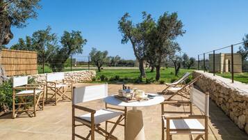 An outdoor patio with stone flooring, wooden furniture, and a view of the countryside.