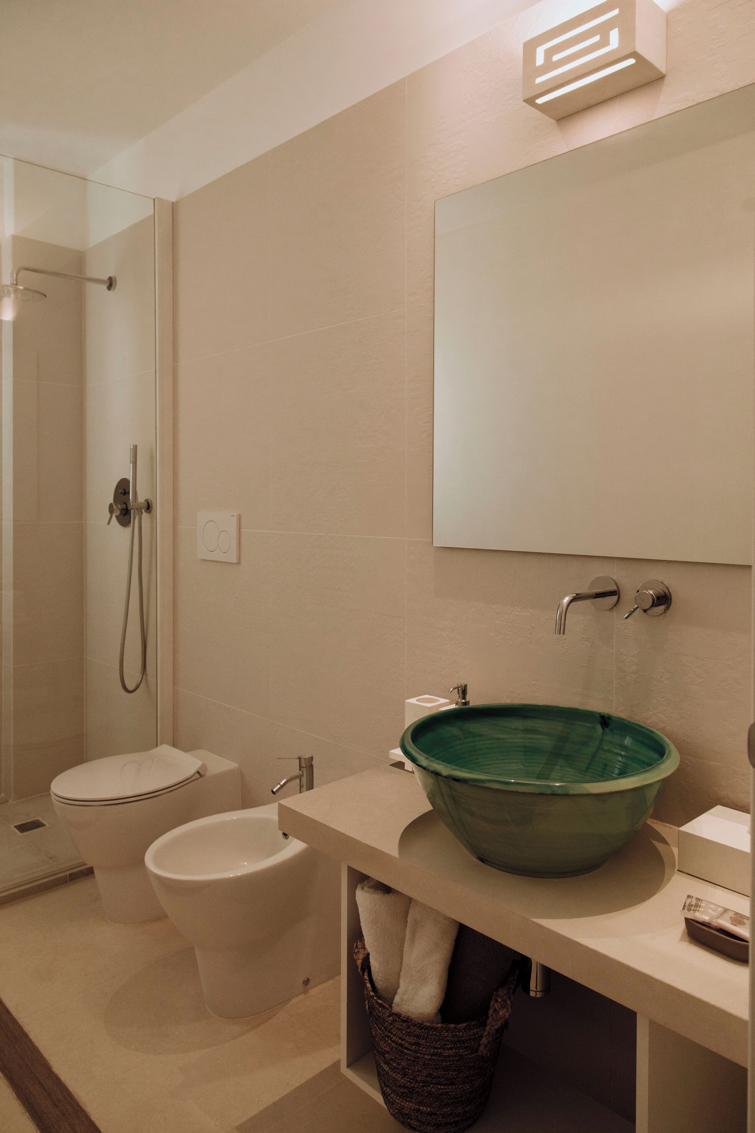 Un baño moderno con ducha acristalada, inodoro blanco, bidé y lavamanos de cerámica verde.