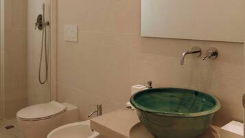 Un baño moderno con ducha acristalada, inodoro blanco, bidé y lavamanos de cerámica verde.