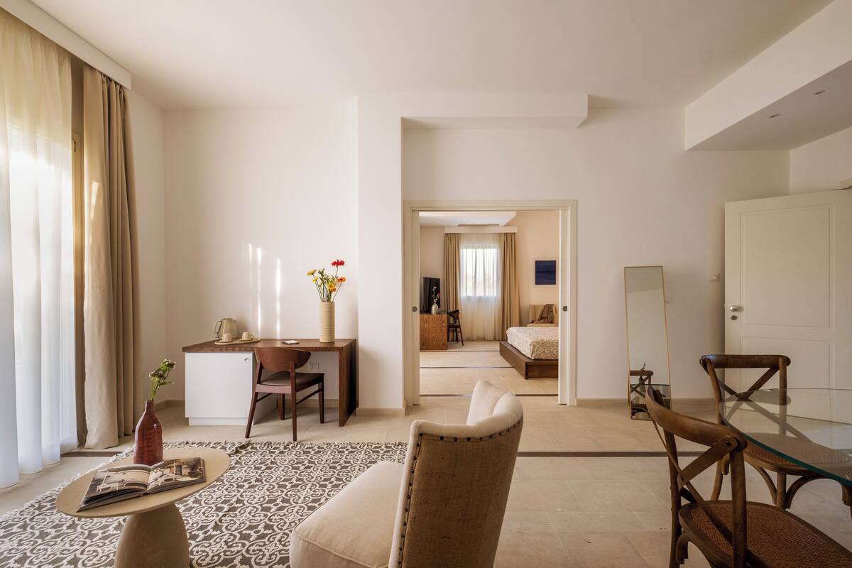 A hotel room with a bed, a desk, a chair, a coffee table, and a mirror.