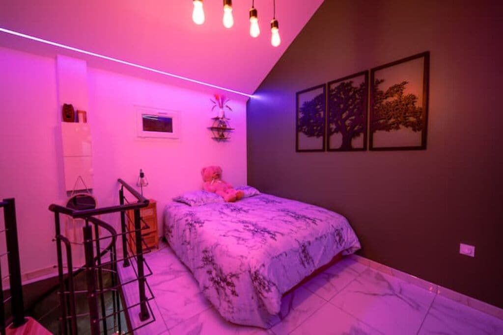 Een slaapkamer met een bed, een bureau en een stoel. Er zijn wandplanken en een raam.