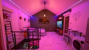 A compact living space with a bed, a TV, a washing machine, and a staircase. - Salle D'amour L'elixird'amour (Étampes-sur-Marne)