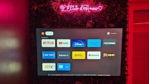 A television screen displaying various streaming service icons, set against a red-lit background with a decorative wall. - Salle D'amour L'elixird'amour (Étampes-sur-Marne)