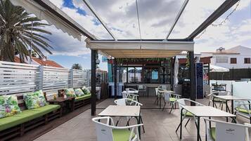 Un patio al aire libre con mesas y sillas, una zona de estar techada y vista a la calle.