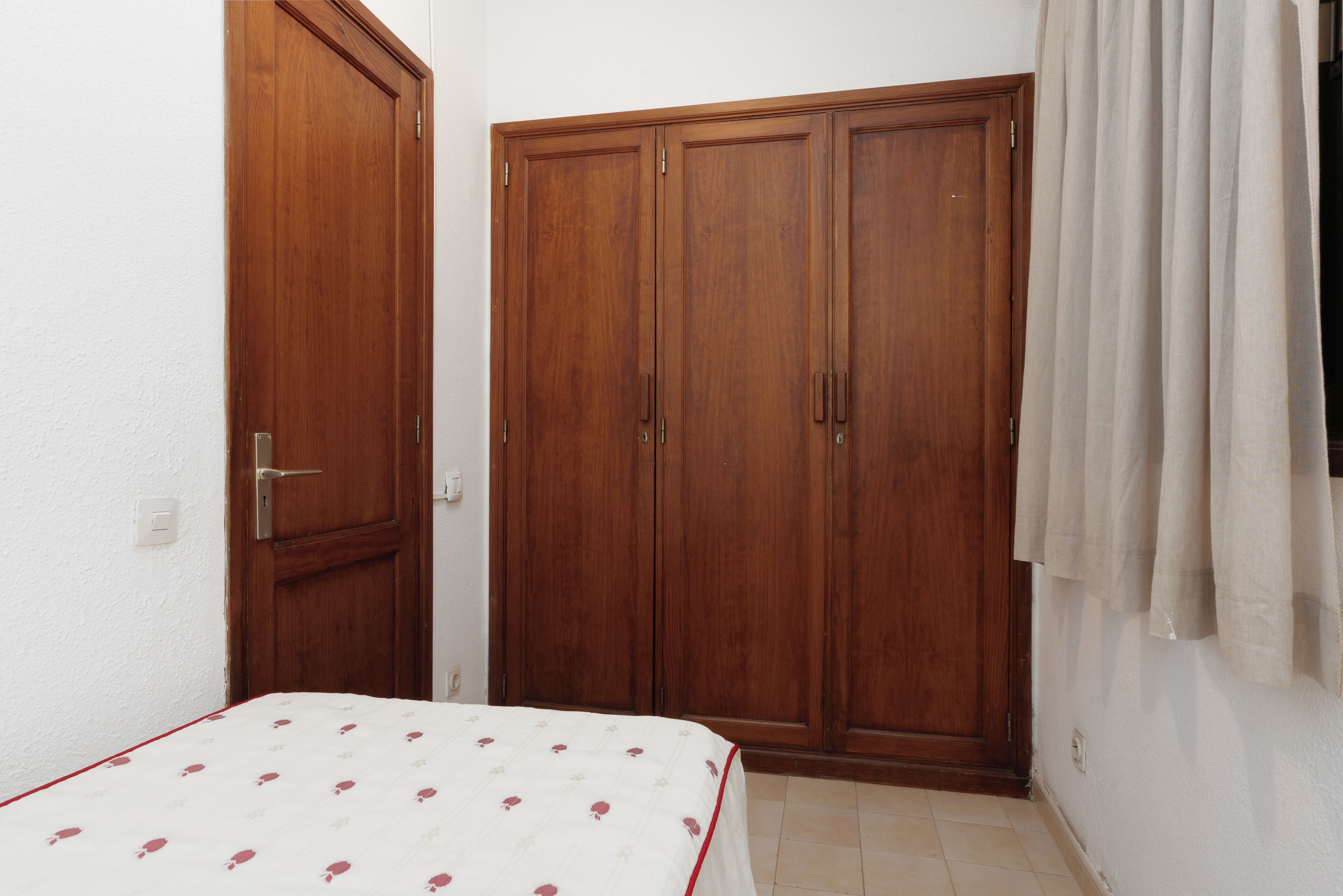 Un dormitorio con cama, armario y cortina.
