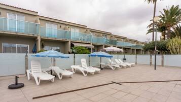 A hotel with multiple balconies, outdoor seating with umbrellas, and a tiled patio area.