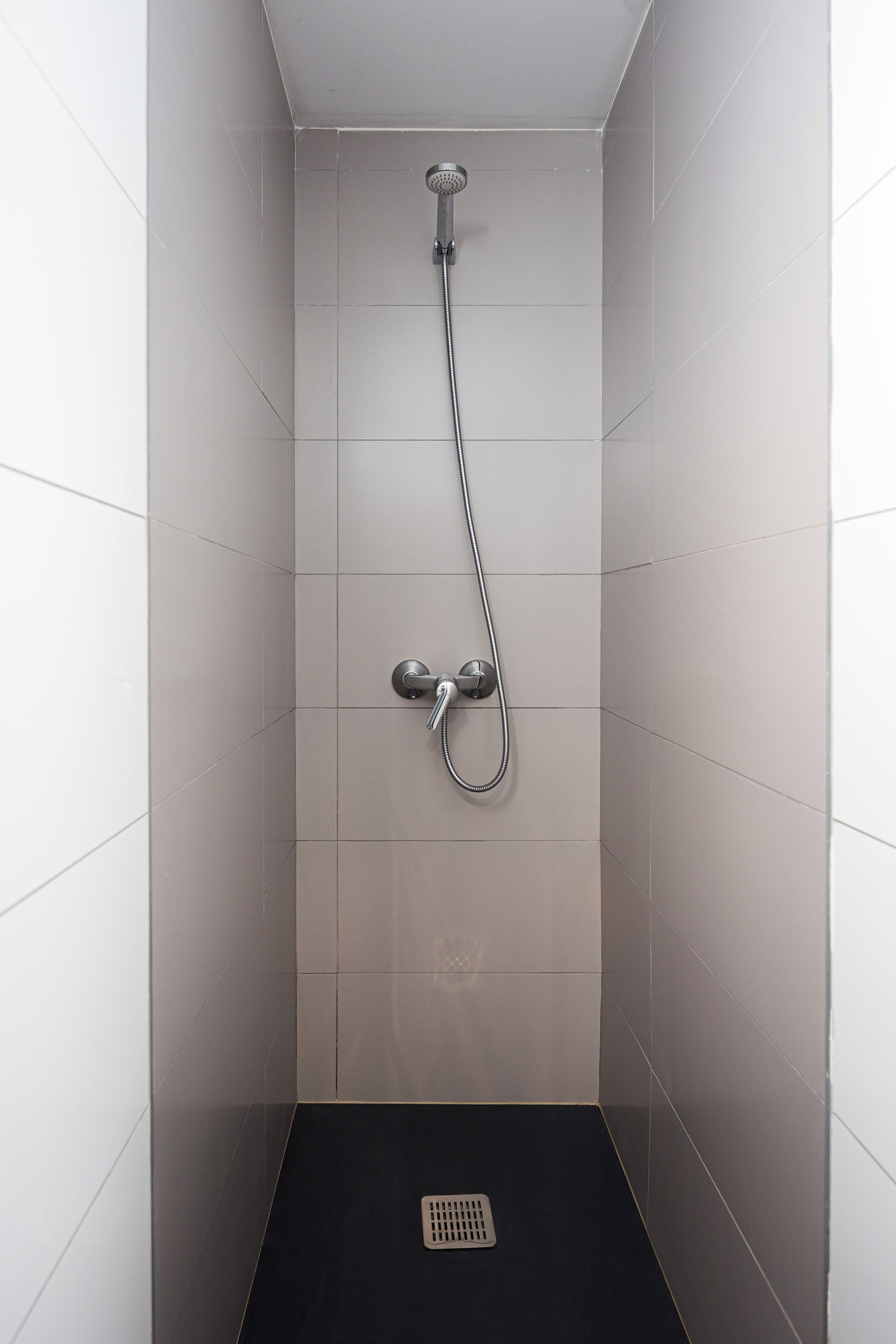A small, enclosed shower area with a showerhead and control knobs, tiled walls, and a black floor.
