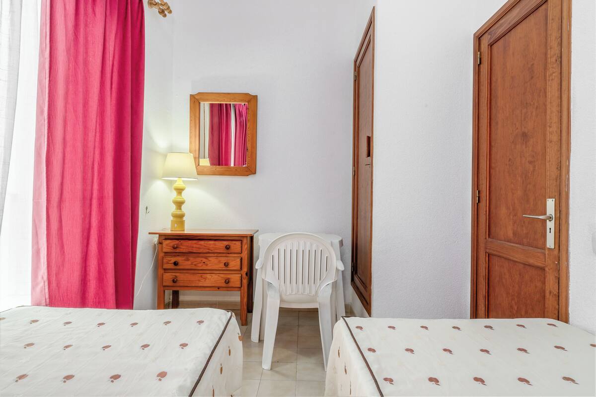A bedroom with two beds, a wooden dresser, a chair, a mirror, and a door.
