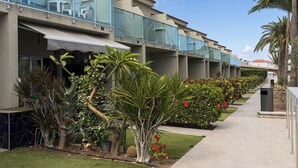 Un hotel con varios balcones, mobiliario exterior y un jardín bien cuidado con diversas plantas y flores.