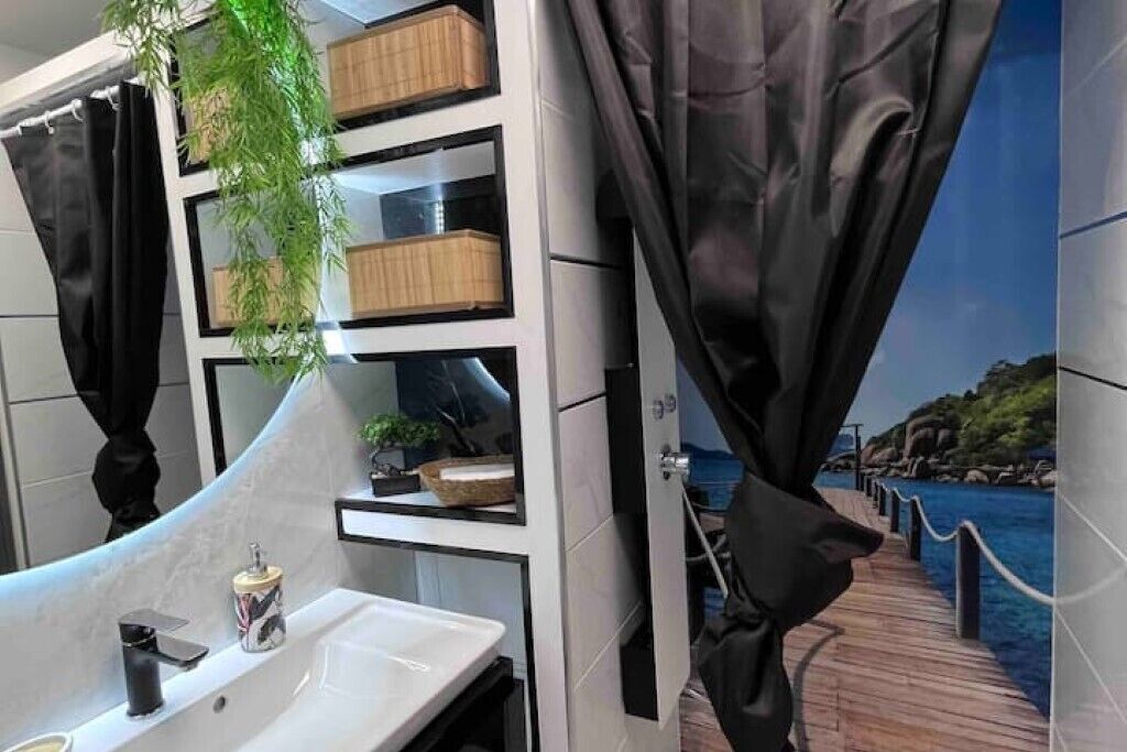 Un baño con un lavabo blanco, cortinas negras y estantes con cajas de madera.