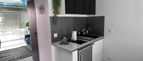A compact kitchen with a modern design, featuring a black upper cabinet, a stainless steel sink, and a small countertop.