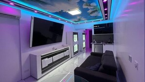 Ein modernes Wohnzimmer mit einem großen Flachbildfernseher, einem schwarzen Sofa und einem Glastisch.
