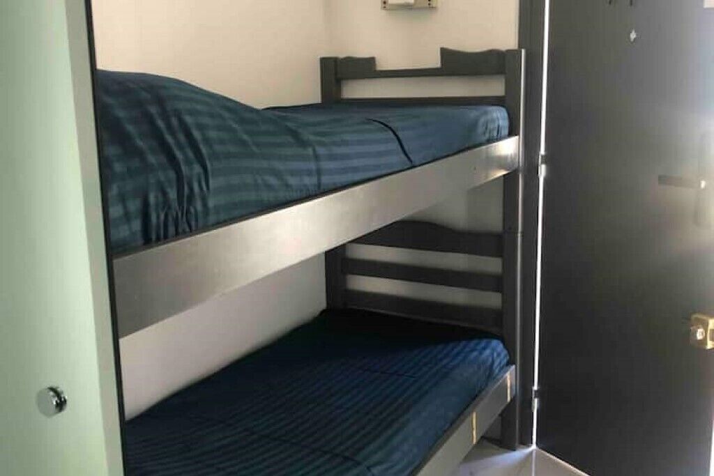 Habitación con literas, una puerta y un estante pequeño sobre la camilla superior.