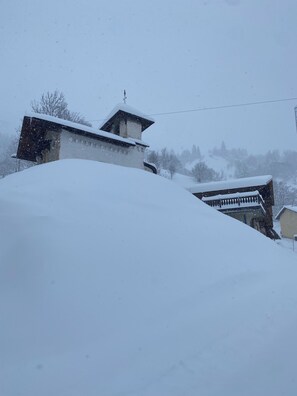 A building with a sloped roof and a visible chimney, surrounded by snow-covered terrain. - Chalet Jusqu' à 18 Couchages Proche des Stations Les Saisies et Les Contamines (Hauteluce)