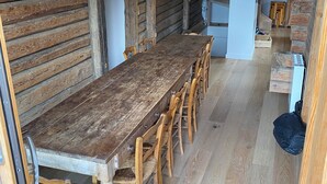 Un comedor rústico de madera con una mesa larga y sillas, una escalera y una zona de cocina.