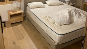 Un dormitorio con techo de madera, una cama con ropa de cama blanca, una mesita de noche con lámpara y una ventana con marco de madera.