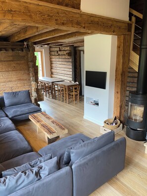 A modern living room with a sectional sofa, a wooden coffee table, a fireplace, and a dining area with wooden chairs.