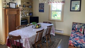 A dining area with a table, chairs, a chandelier, a fireplace, a television, and a window with curtains. - Historic Hillside Vacation Home (Twillingate)