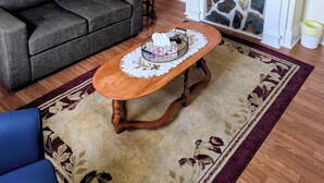 A living room with a sofa, a table with a tray, a fireplace, a fan, and a wall-mounted mirror. - Historic Hillside Vacation Home (Twillingate)