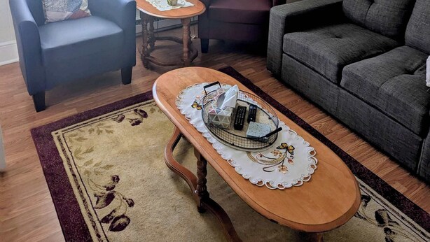 A living room with a sofa, armchair, and a small table with a lamp. - Historic Hillside Vacation Home (Twillingate)