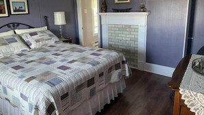 A bedroom with a bed, a fireplace, and a nightstand. - Historic Hillside Vacation Home (Twillingate)