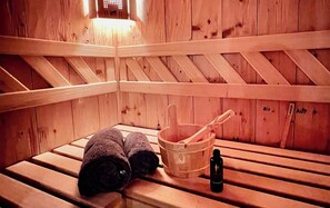 Un sauna en bois avec des bancs, un seau en bois et des serviettes enroulées.