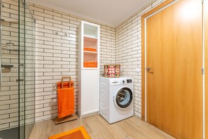 Een wasserette met een wasmachine, een glazen douchecabine en een houten deur.