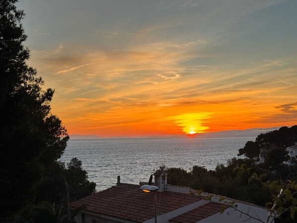 Een zonsondergang boven de zee met uitzicht op een kustgebied en gebouwen.