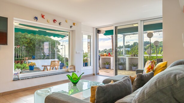 A modern living room with a glass coffee table, grey sofa, and a view of a balcony with potted plants. - Beach Front Luxury Designer Two Bedroom Apartment (CT)