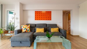A modern living room with a grey sectional sofa, a glass coffee table, and a vibrant orange wall art piece. - Beach Front Luxury Designer Two Bedroom Apartment (CT)