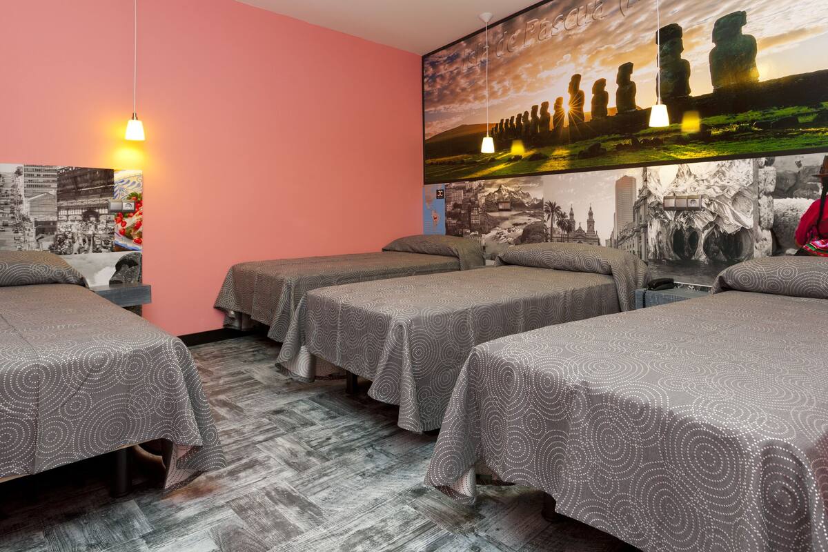 A hotel room with four single beds, a large mural of Easter Island statues, and a cityscape poster on the wall.