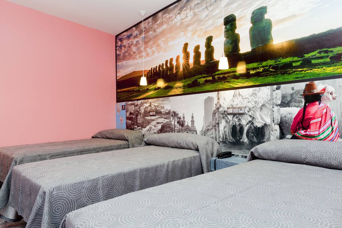 A hotel room with two single beds, a large mural of Easter Island statues, and a wall-mounted TV.