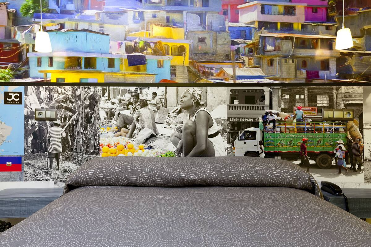 A bed with a patterned bedspread, a wall with a colorful mural, and a hanging light fixture.