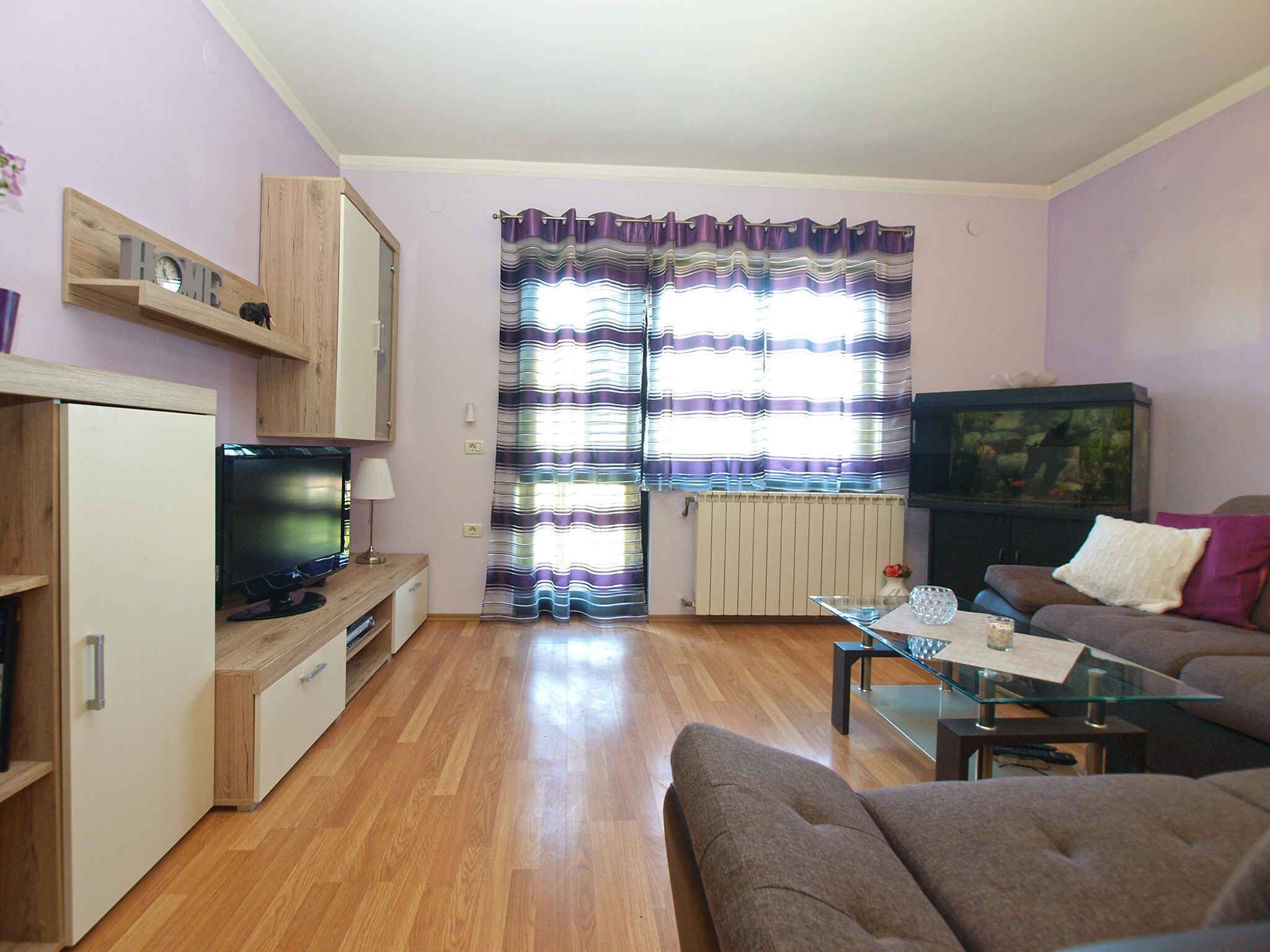 Ein Wohnzimmer mit Fernseher, Sofa und einem Glastisch.